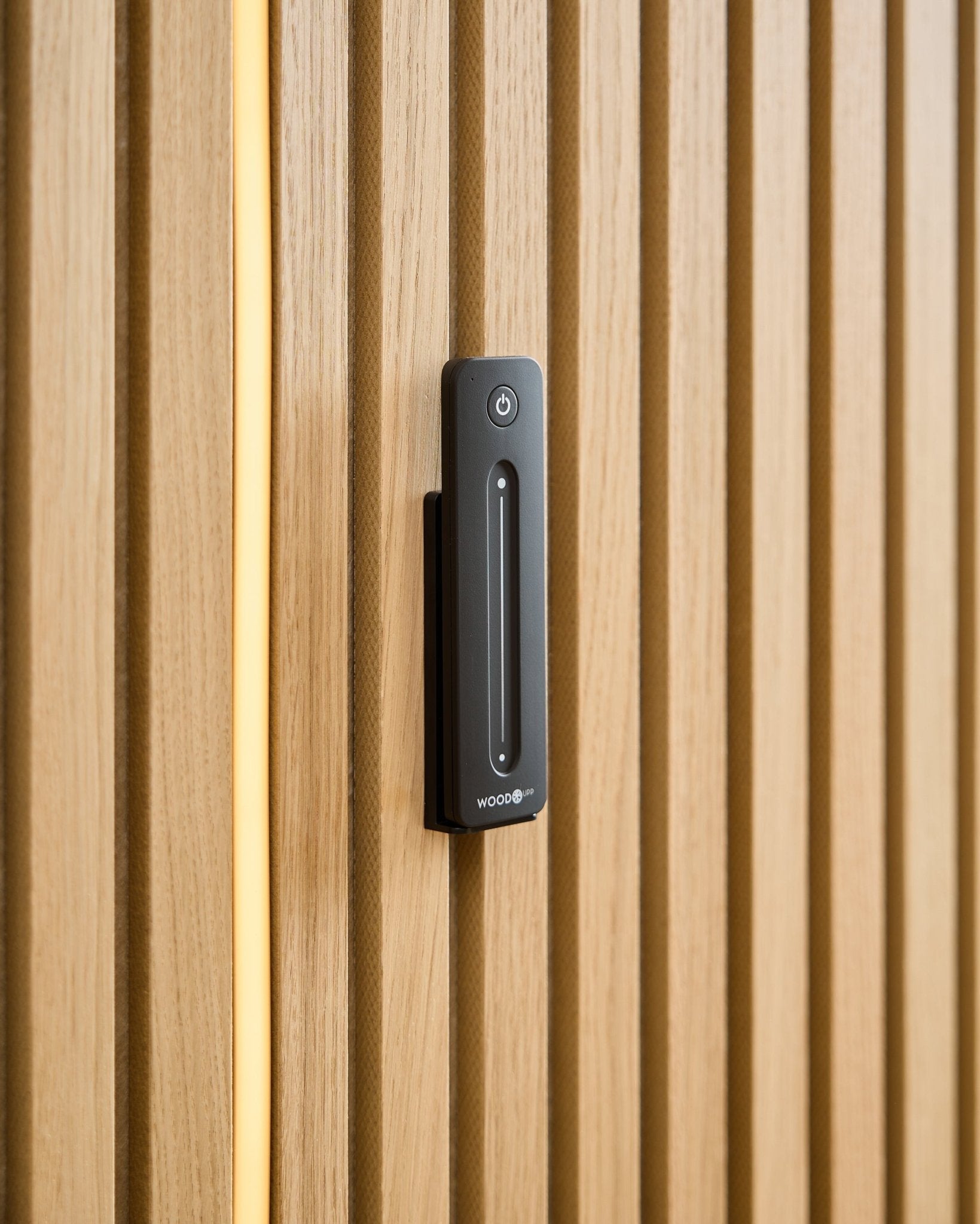 A WoodUpp Lumi | Remote / LED Striplight is installed on a light wood acoustic panel, with a yellow cable visible behind the wooden slats.