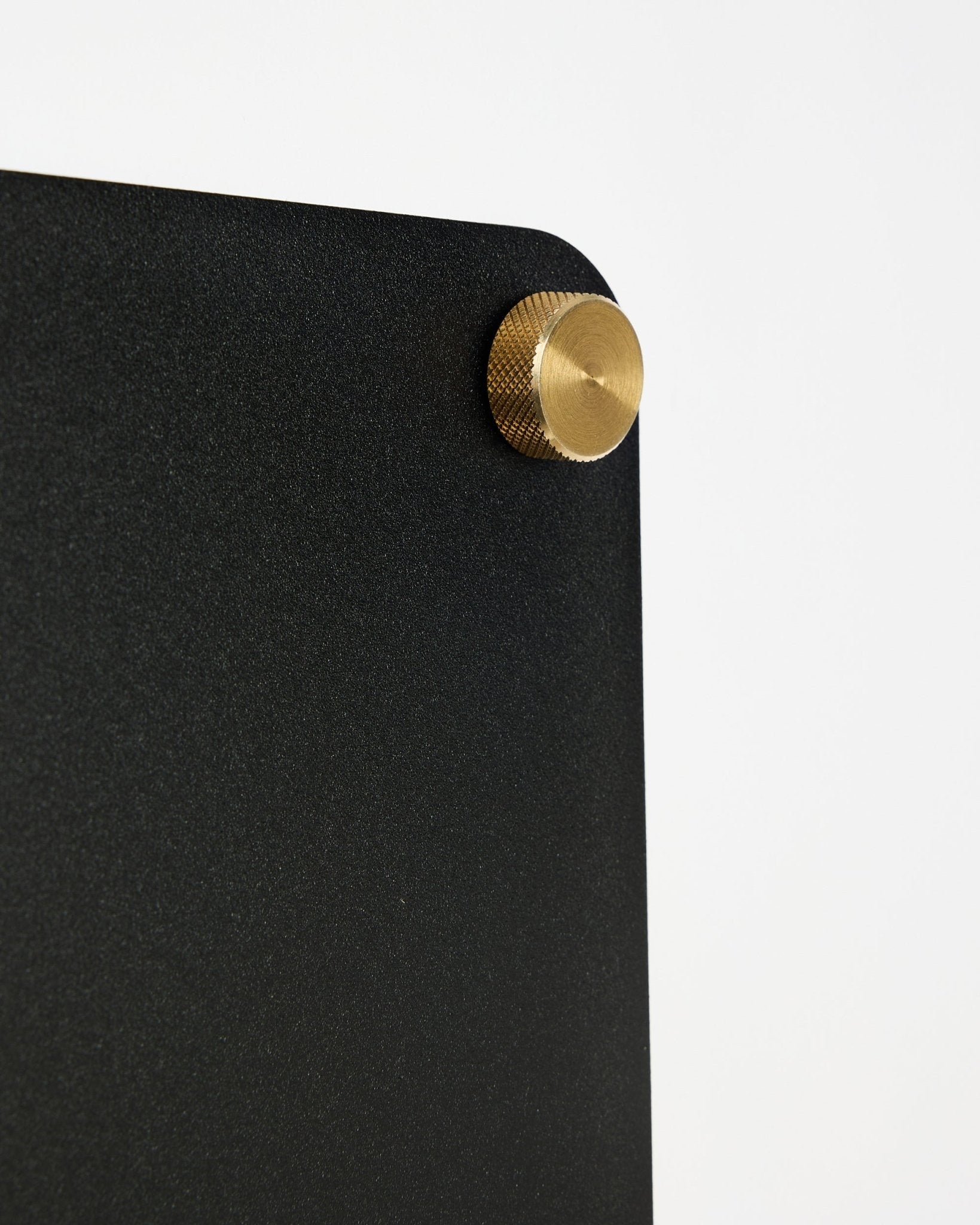 Close-up of WoodUpp Norr black acoustic magnetic board (small) with a rounded corner and gold screw fastener on a white background.