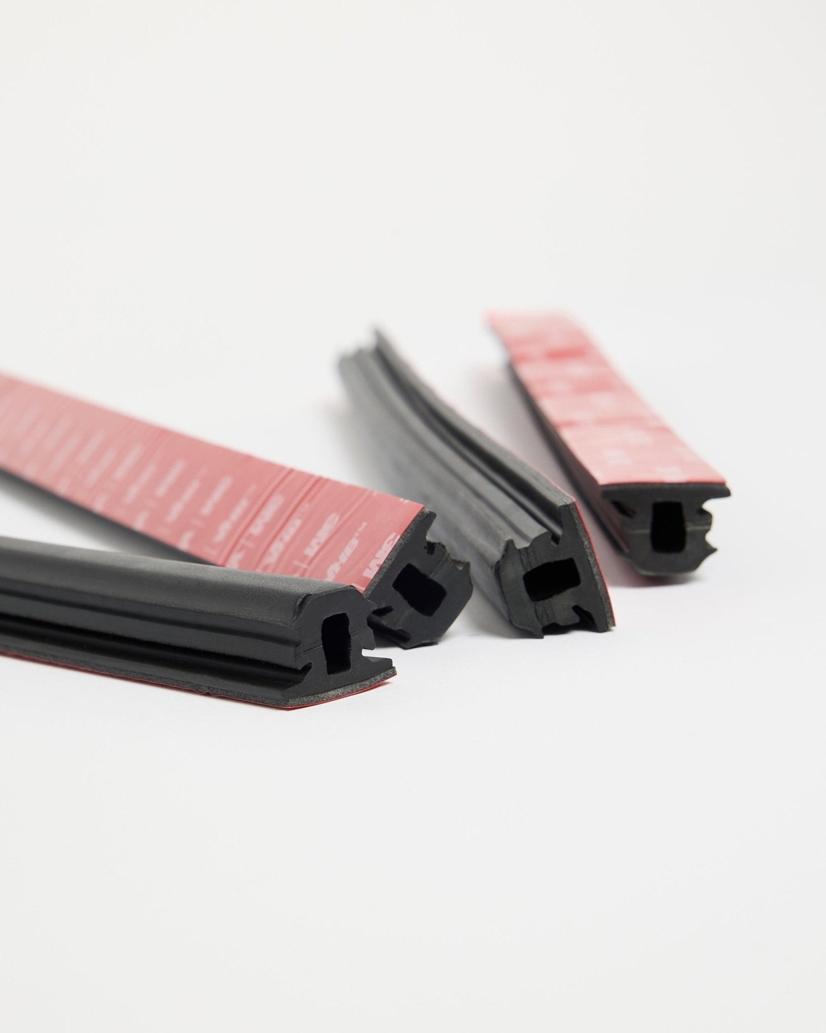 Four WoodUpp Dupps Pop-on Profile black rubber strips with red adhesive, designed for Akupanel installation, laid out on a white surface in various directions.