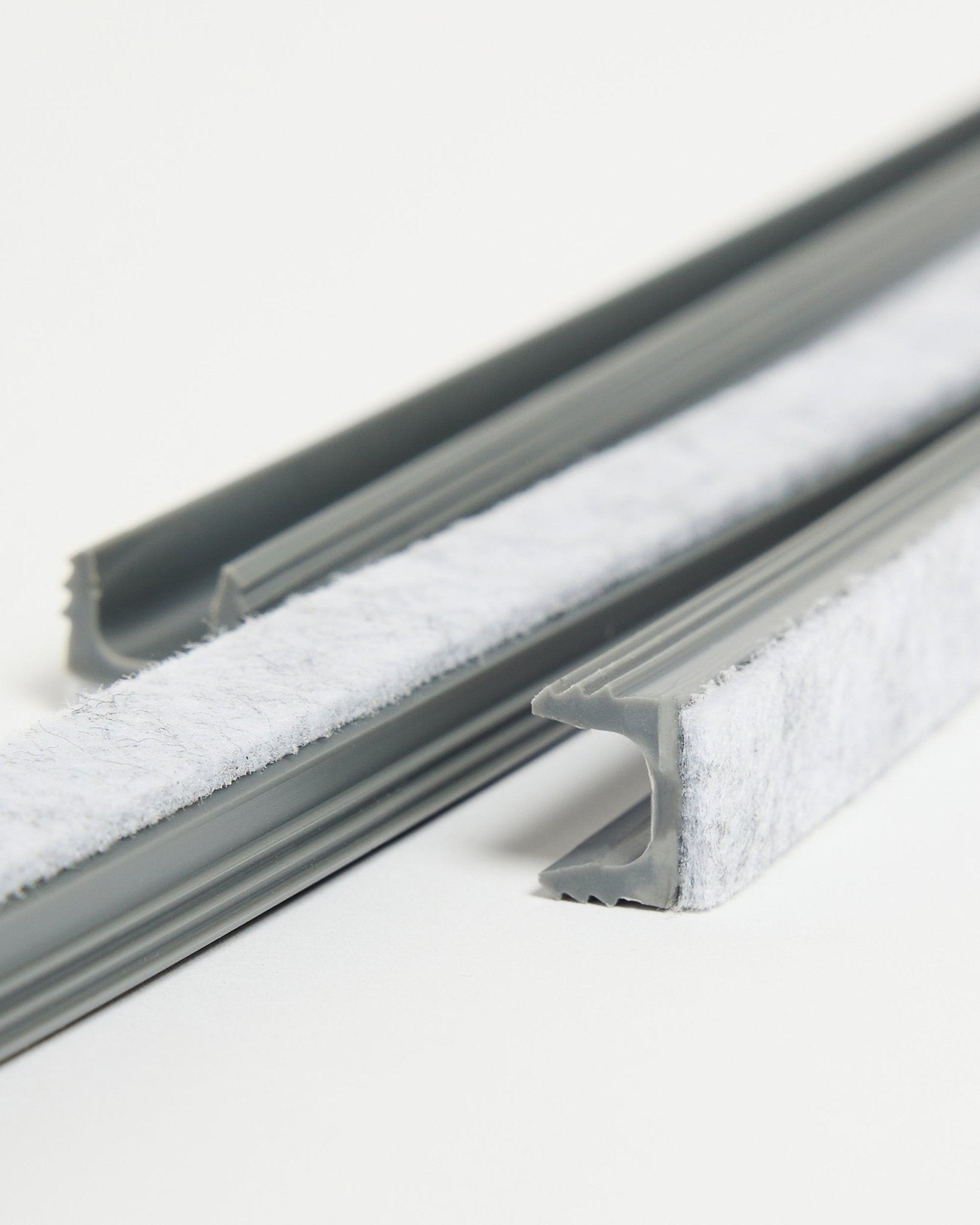 Three gray WoodUpp Dupps Pop-on Cable Covers with white weatherstripping and flexible TPV channels placed on a white surface.