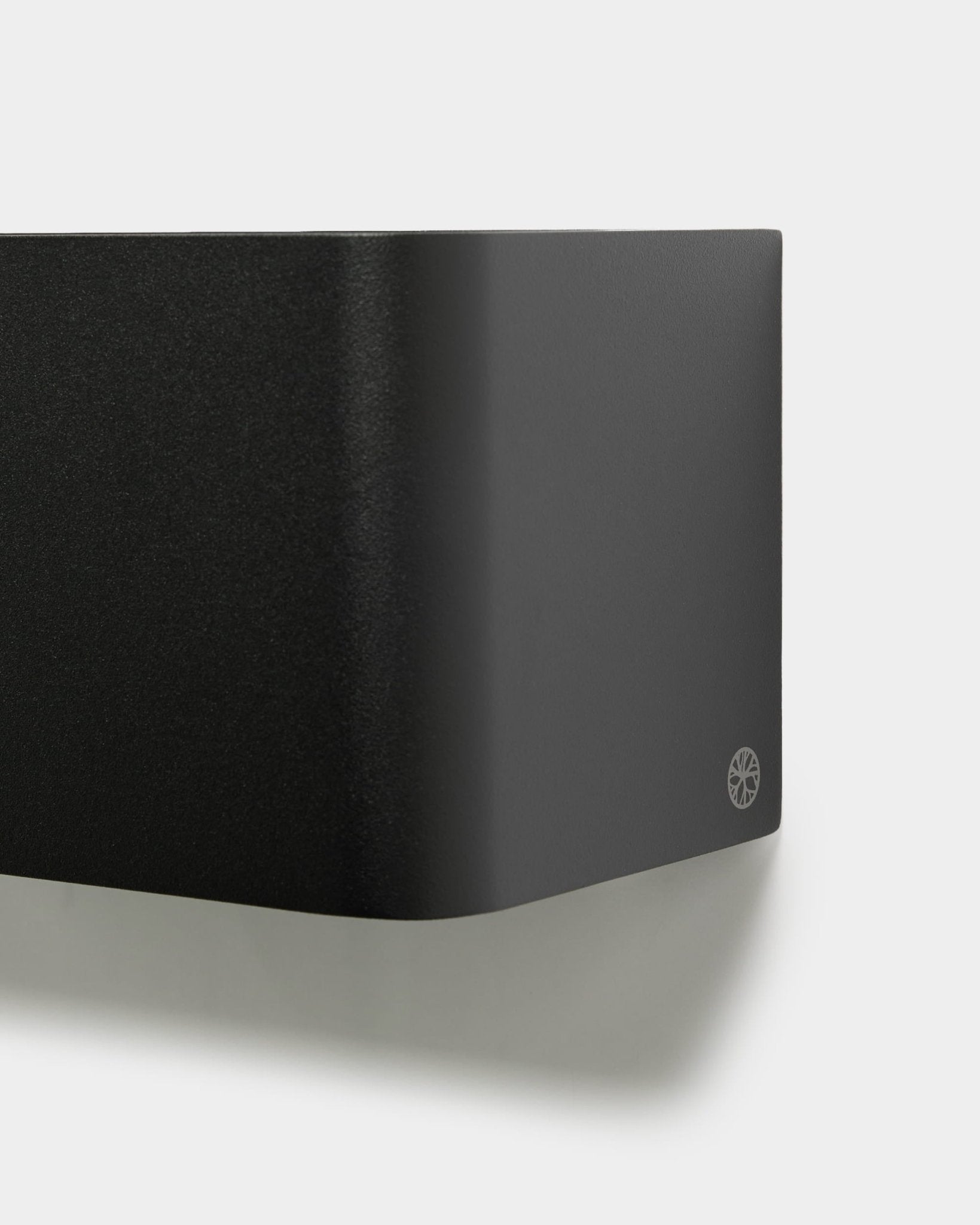 Close-up of the minimalist WoodUpp Norr Plant Box (23.9 cm, black) with rounded edges and logo, mounted on a white wall. Nordic acoustic accessory design.