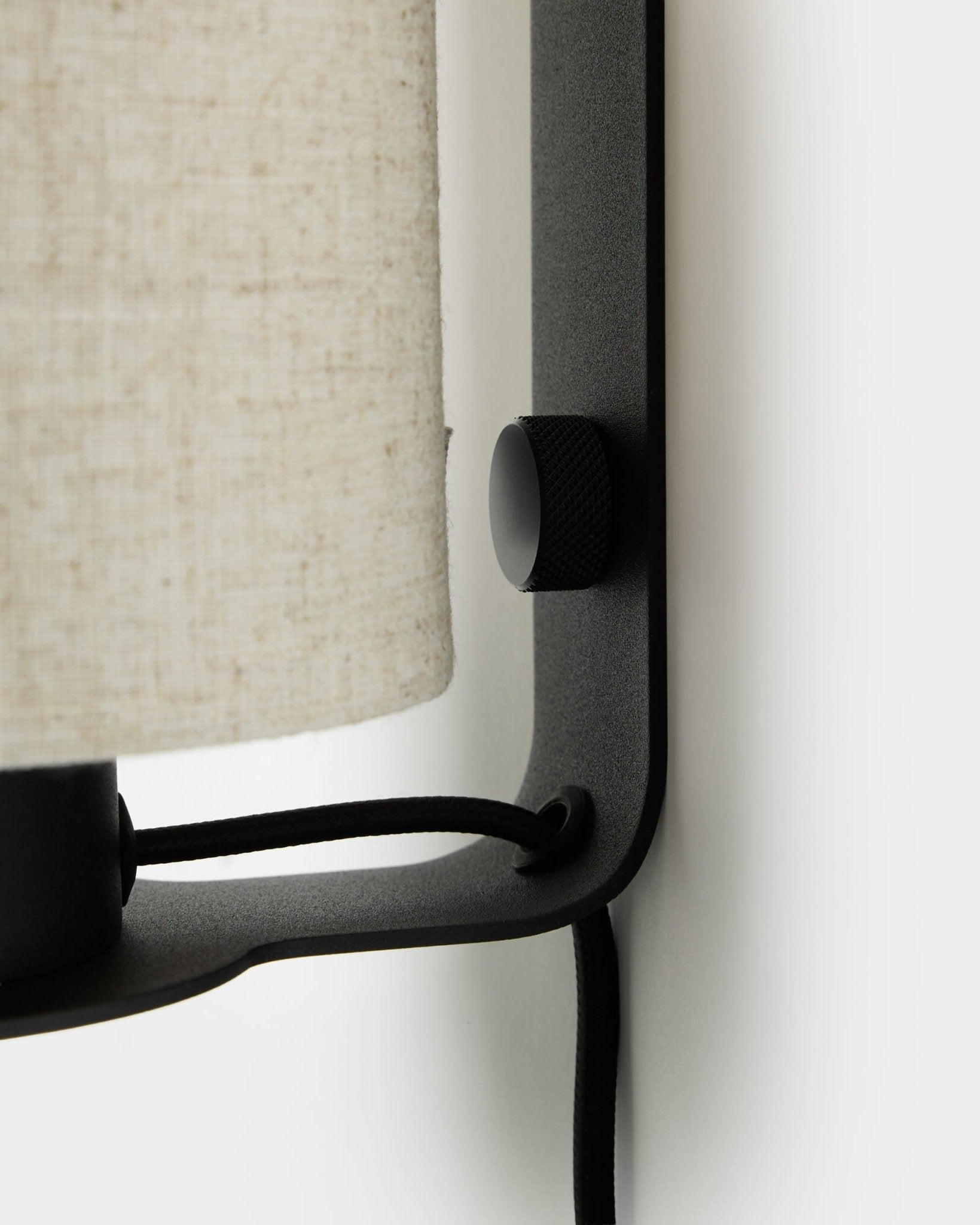Close-up of the WoodUpp Feya Wall Lamp in black and beige, featuring a textured knob, linen-cotton shade, and visible cord mounted on a white wall.