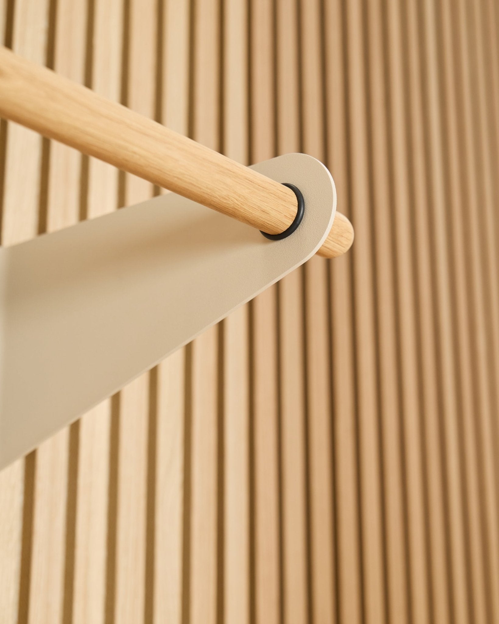 Close-up of the WoodUpp Linn Coat Rail in beige (75.9 cm), mounted on a beige metal bracket against a textured Akupanel acoustic slatwall panel.